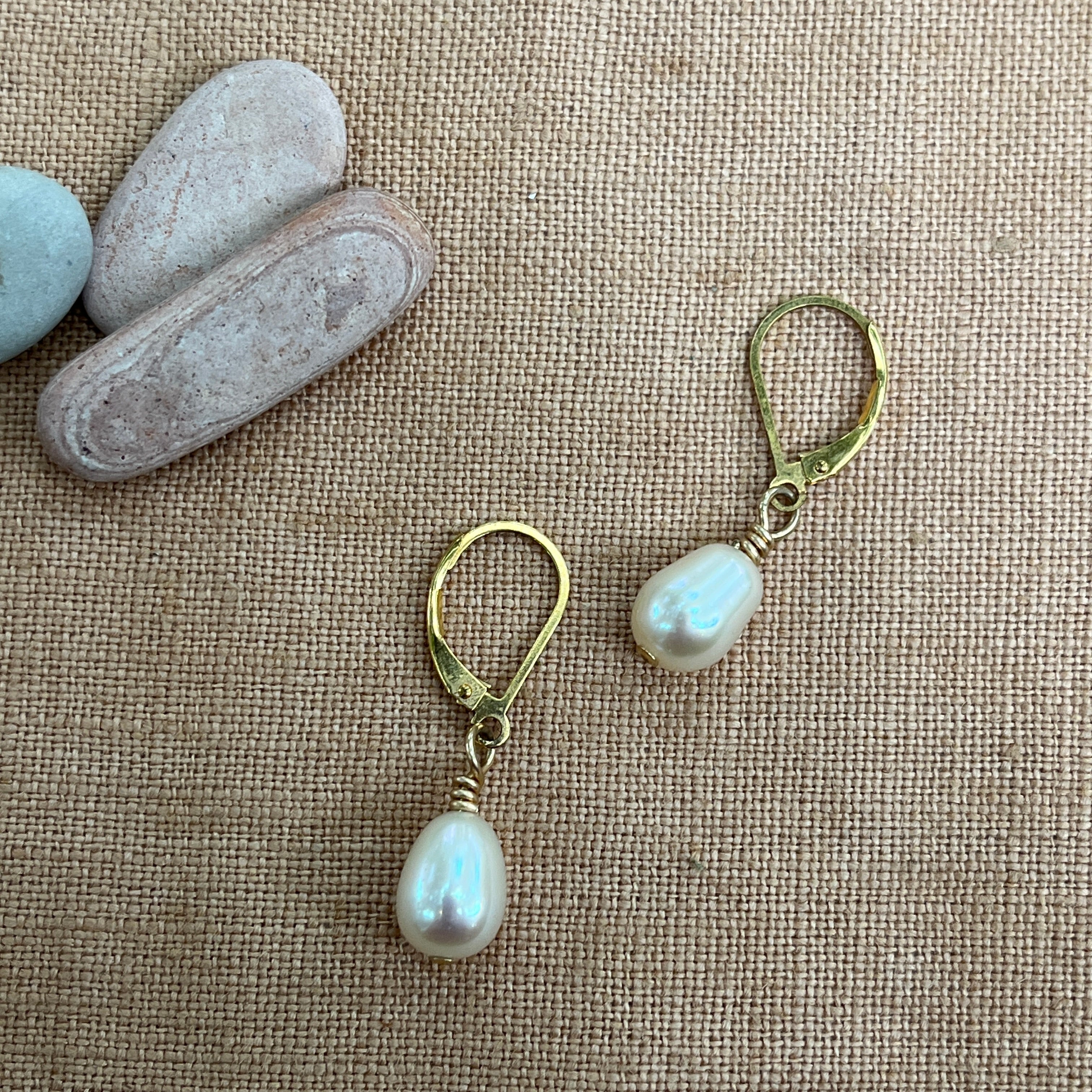 Pearl earrings with gold hooks on a textured beige surface.
