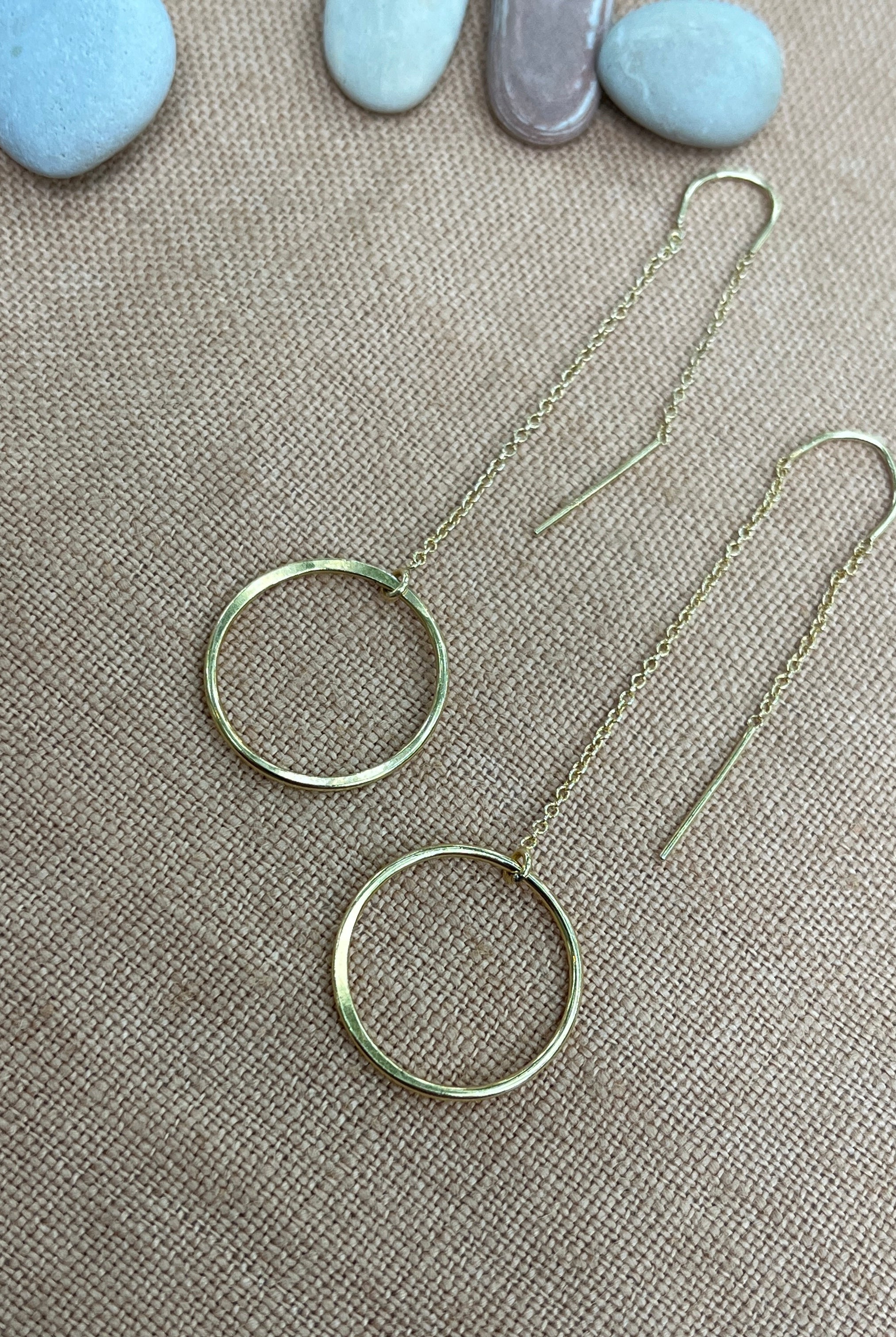 Silver hoop earrings on a textured beige surface with stones in the background