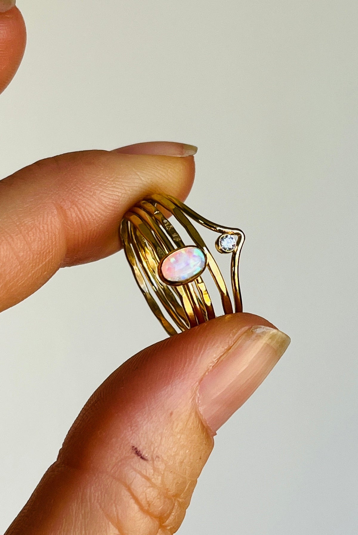 Hand holding a gold ring with an opal stone against a plain background