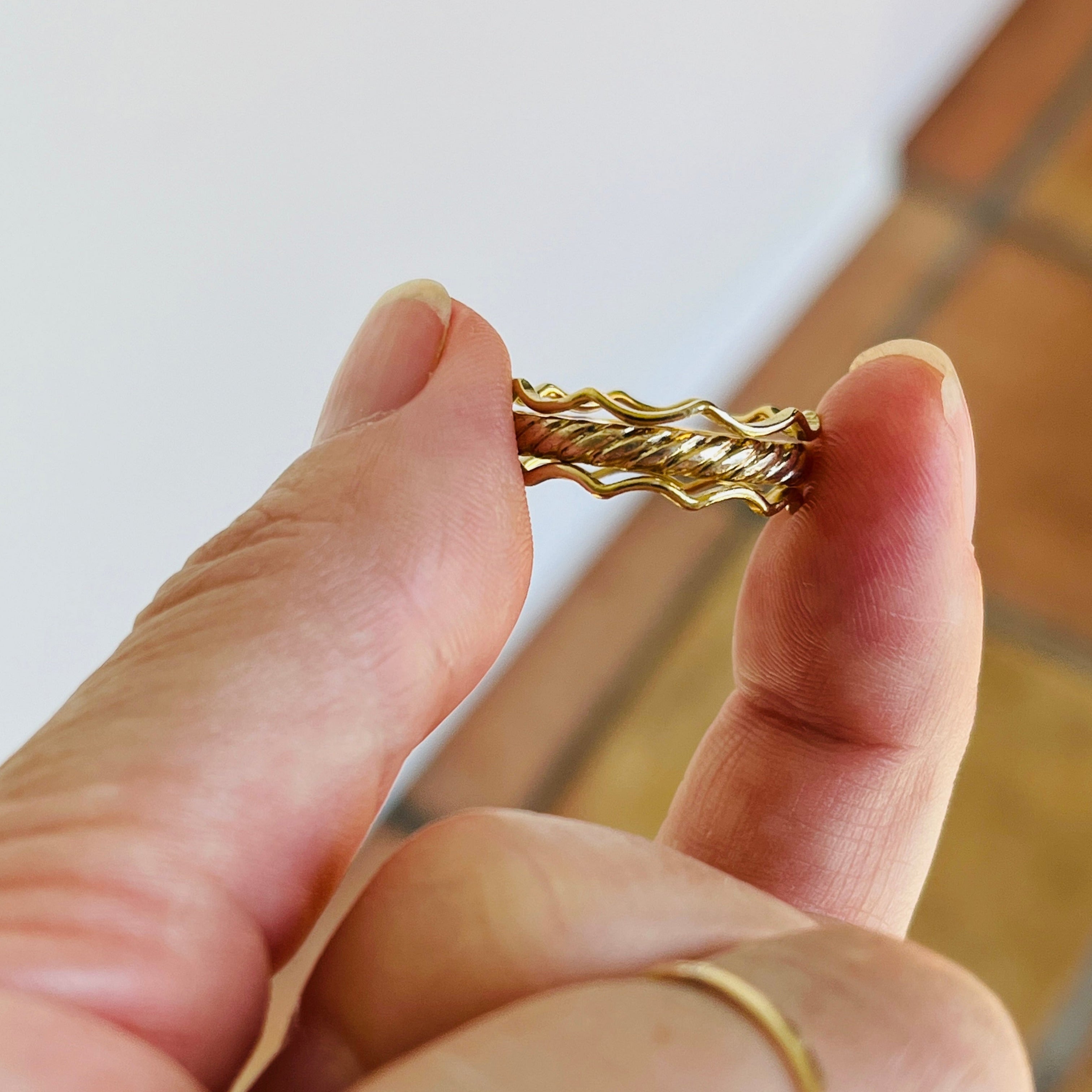 Hand holding a gold bracelet with a blurred background