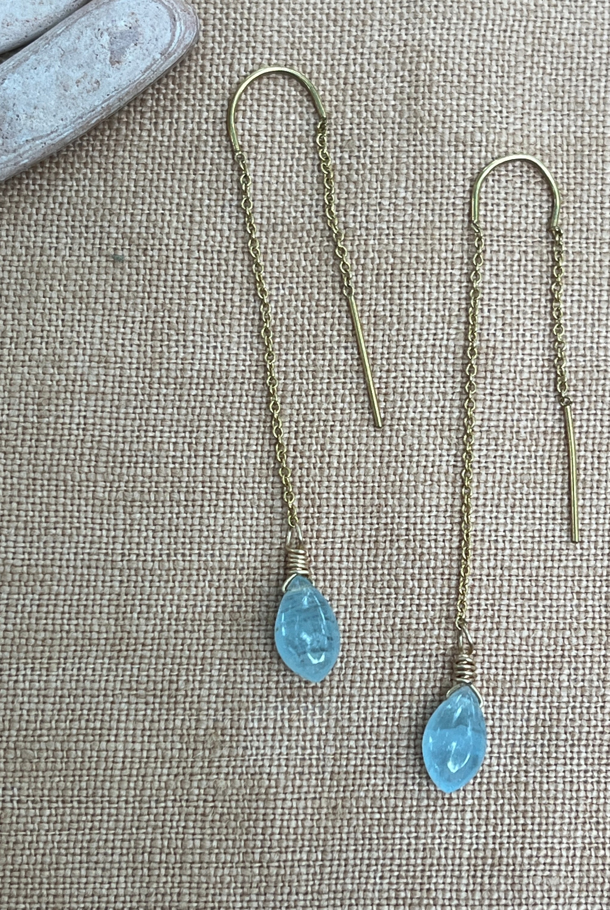 Threader earrings with blue gemstones on a textured fabric background