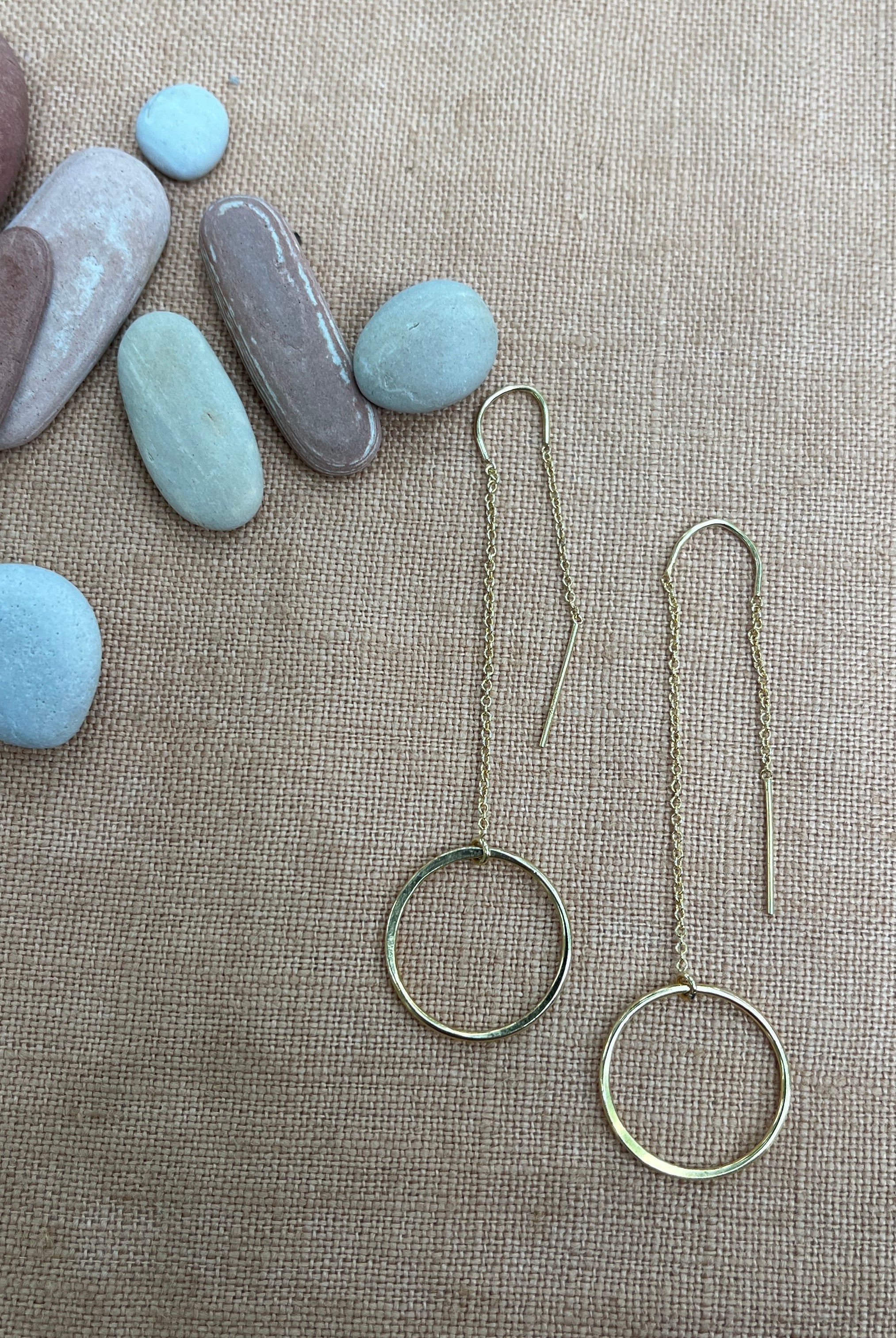 Gold hoop earrings on a textured surface with stones in the background