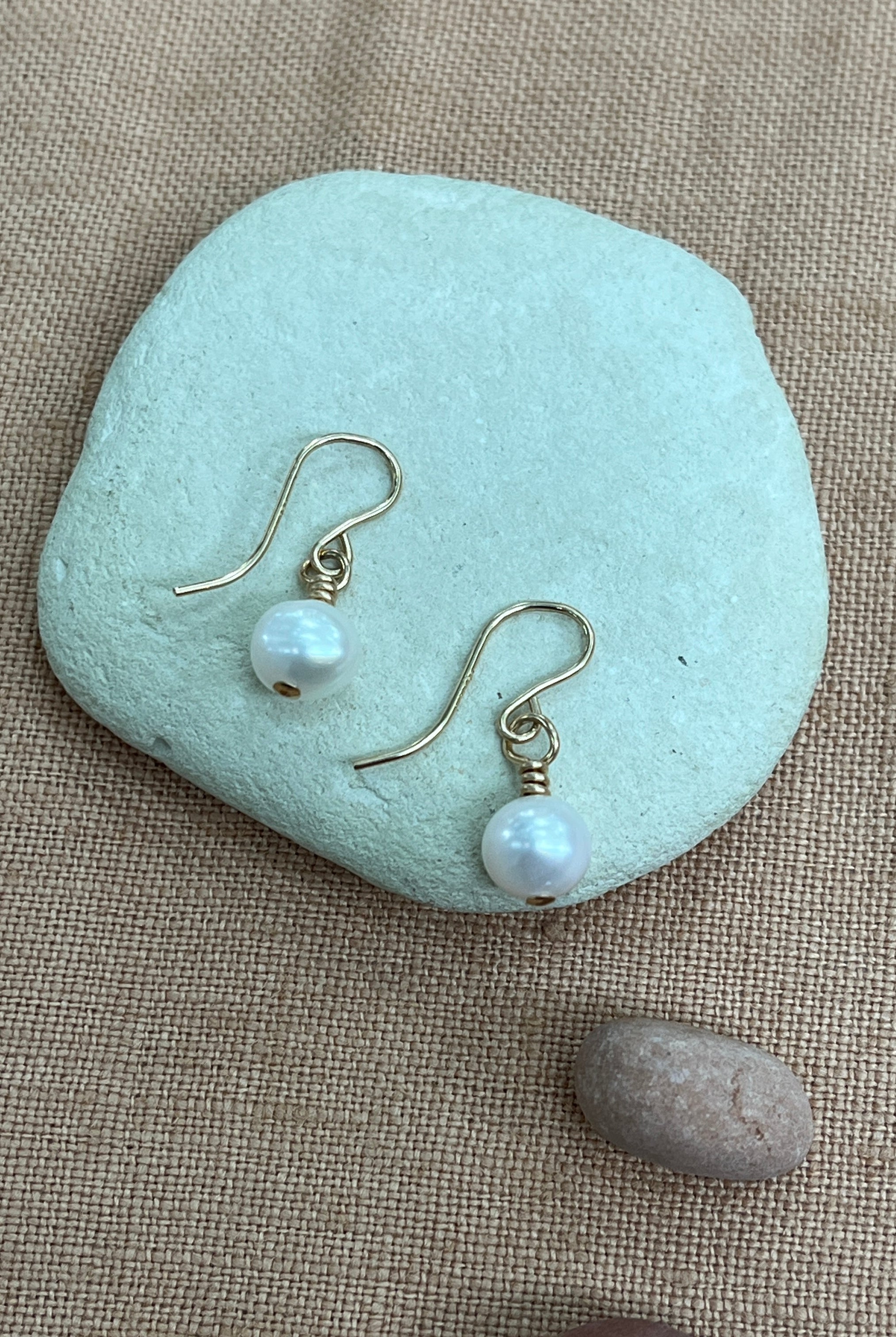 Pearl earrings on a light blue stone with a beige background