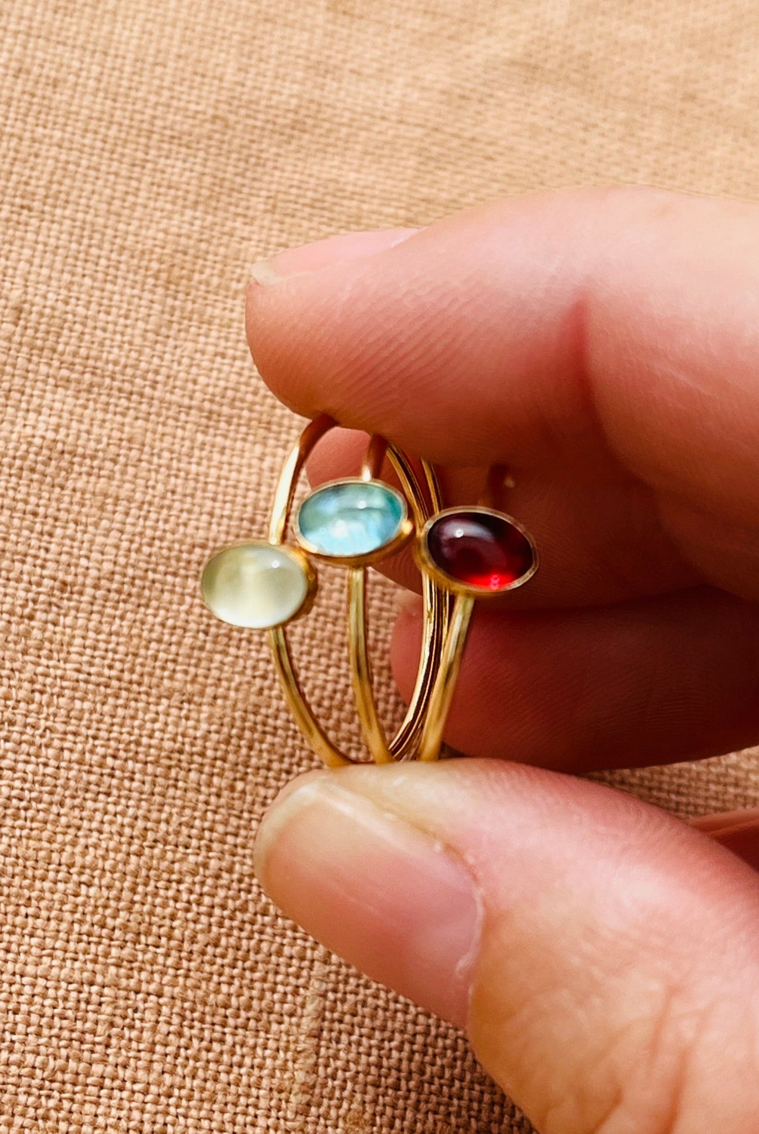 Gold ring with multicolored gemstones held between fingers on a beige fabric background