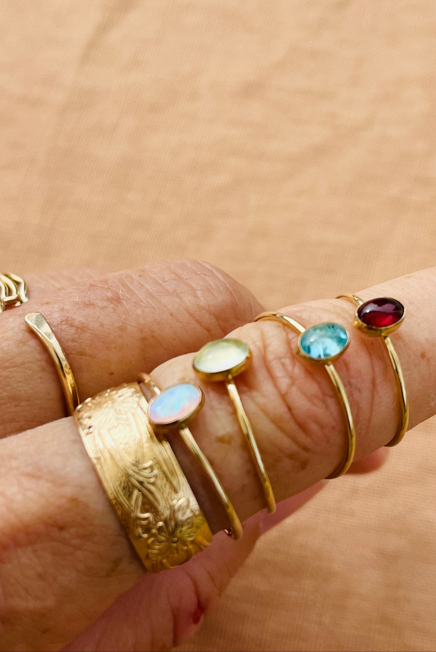 Hand wearing multiple gold rings with gemstones on a beige background