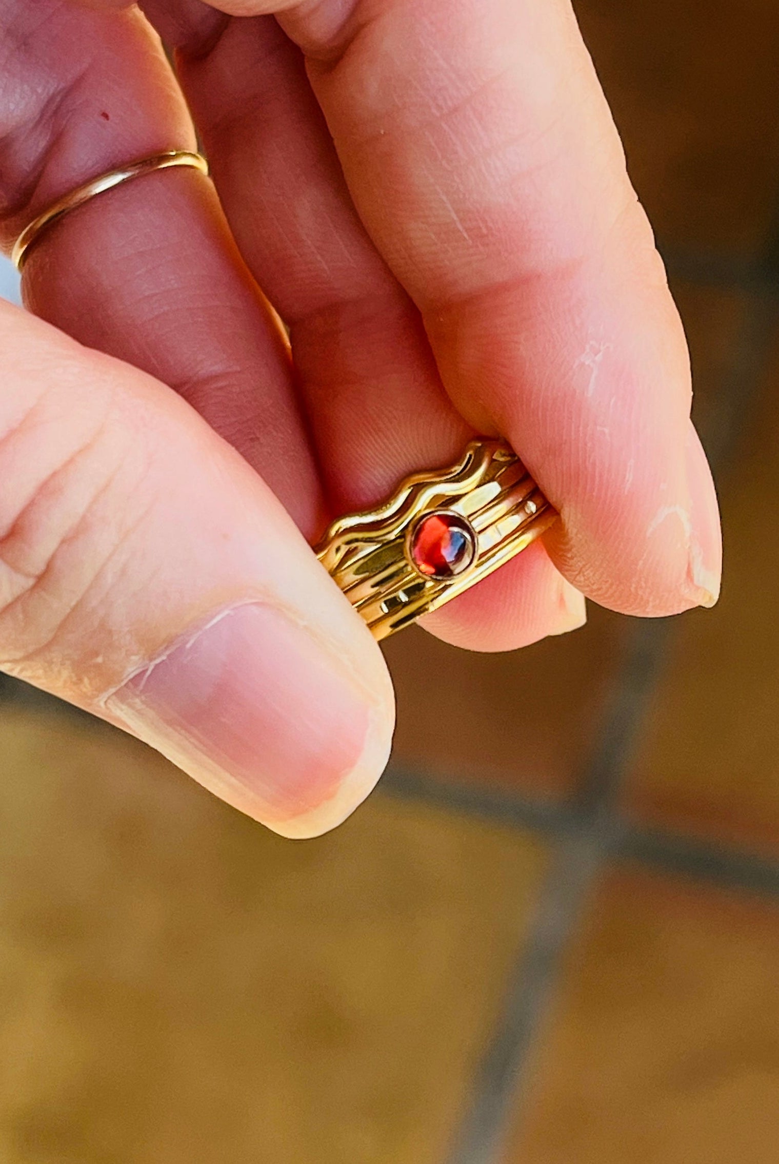 Gold ring with a red gemstone held between fingers on a tiled floor background