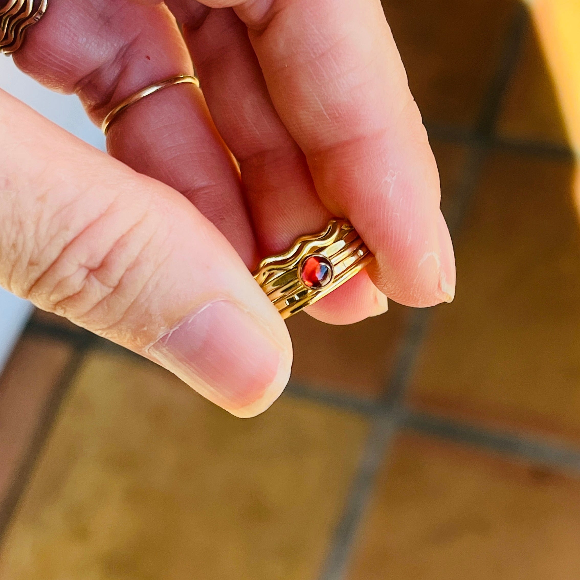 Gold ring with a red gemstone held between fingers on a tiled floor background
