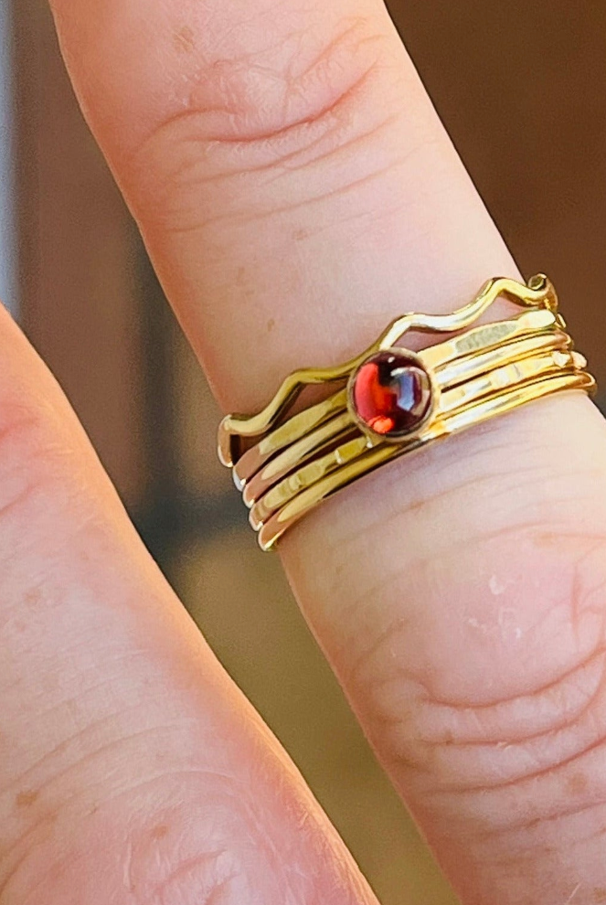 Gold ring with a red gemstone on a finger against a blurred background