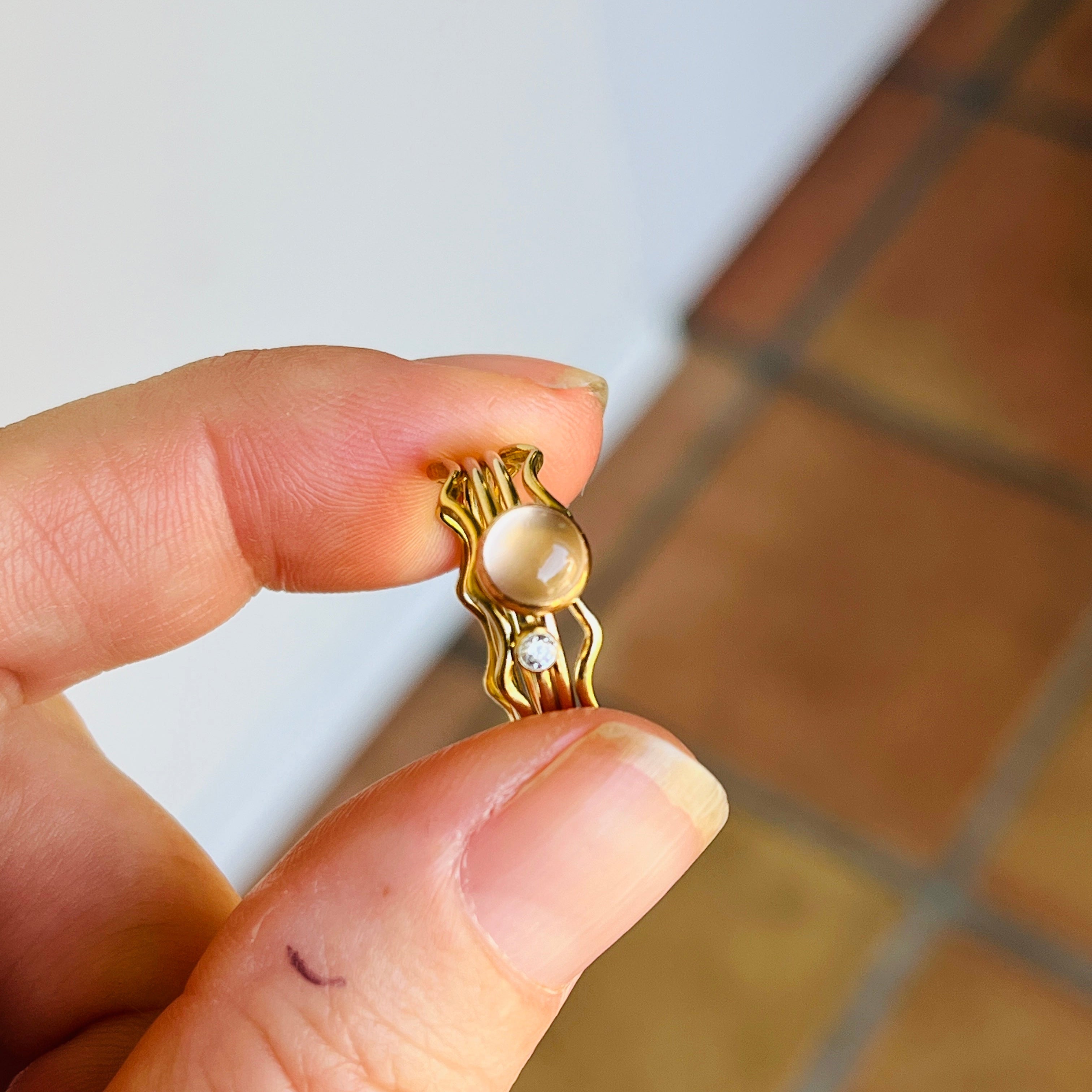 Gold ring with a pearl held between fingers on a tiled floor.