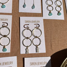 Siren Jewelry gold and turquoise earrings displayed on cards against a brown background.