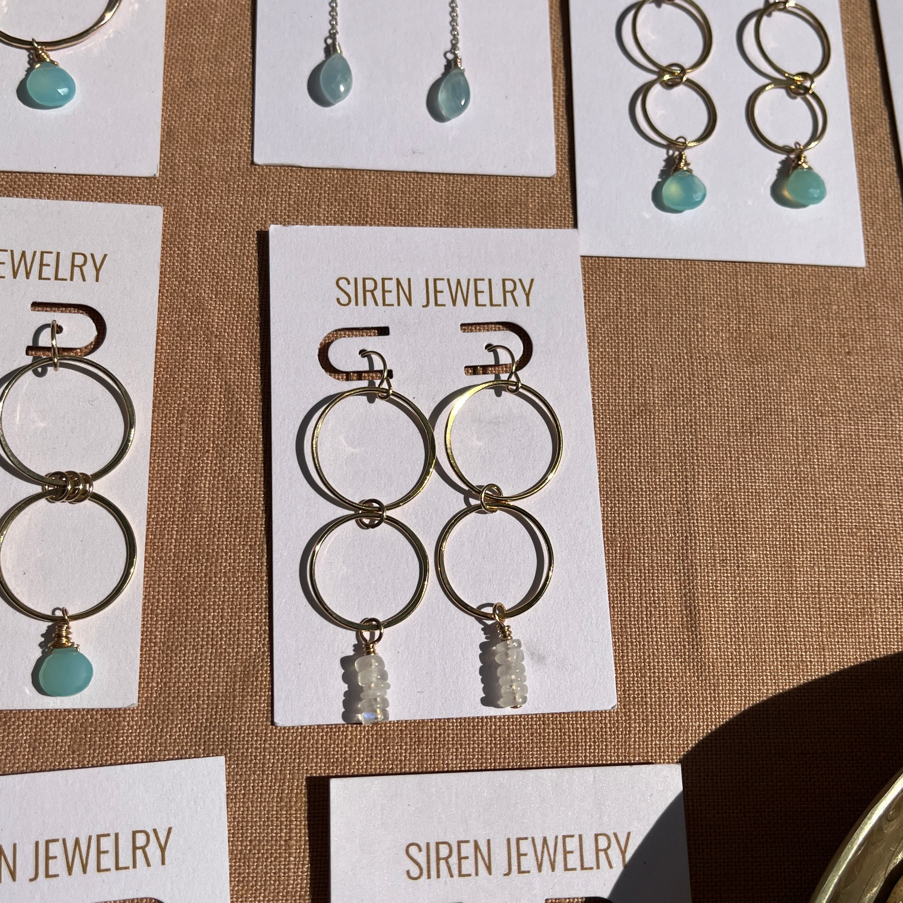 Siren Jewelry gold and turquoise earrings displayed on cards against a brown background.