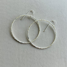Load image into Gallery viewer, a pair of silver hoop earrings sitting on top of a table
