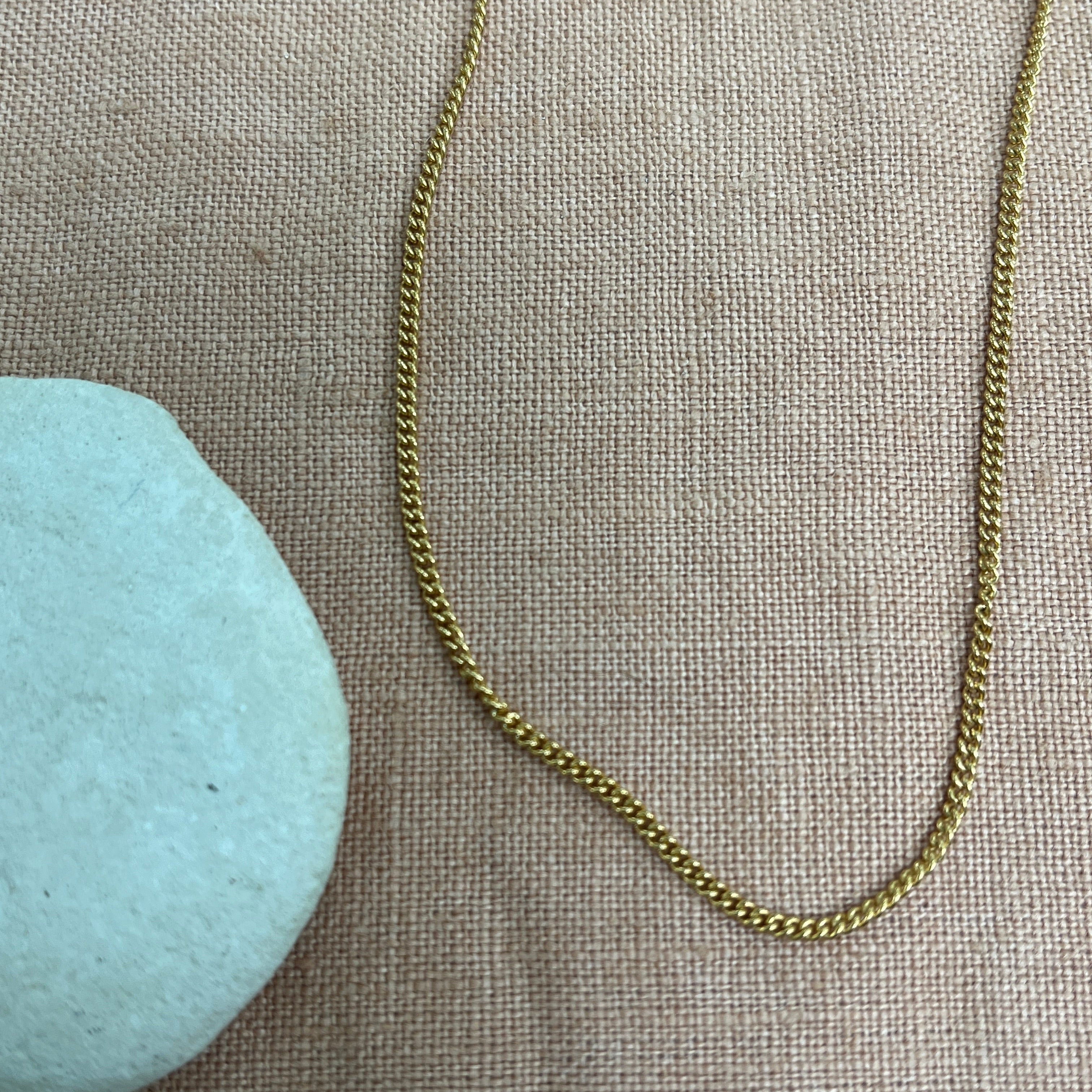 Gold chain necklace on a textured beige surface with a light blue stone.