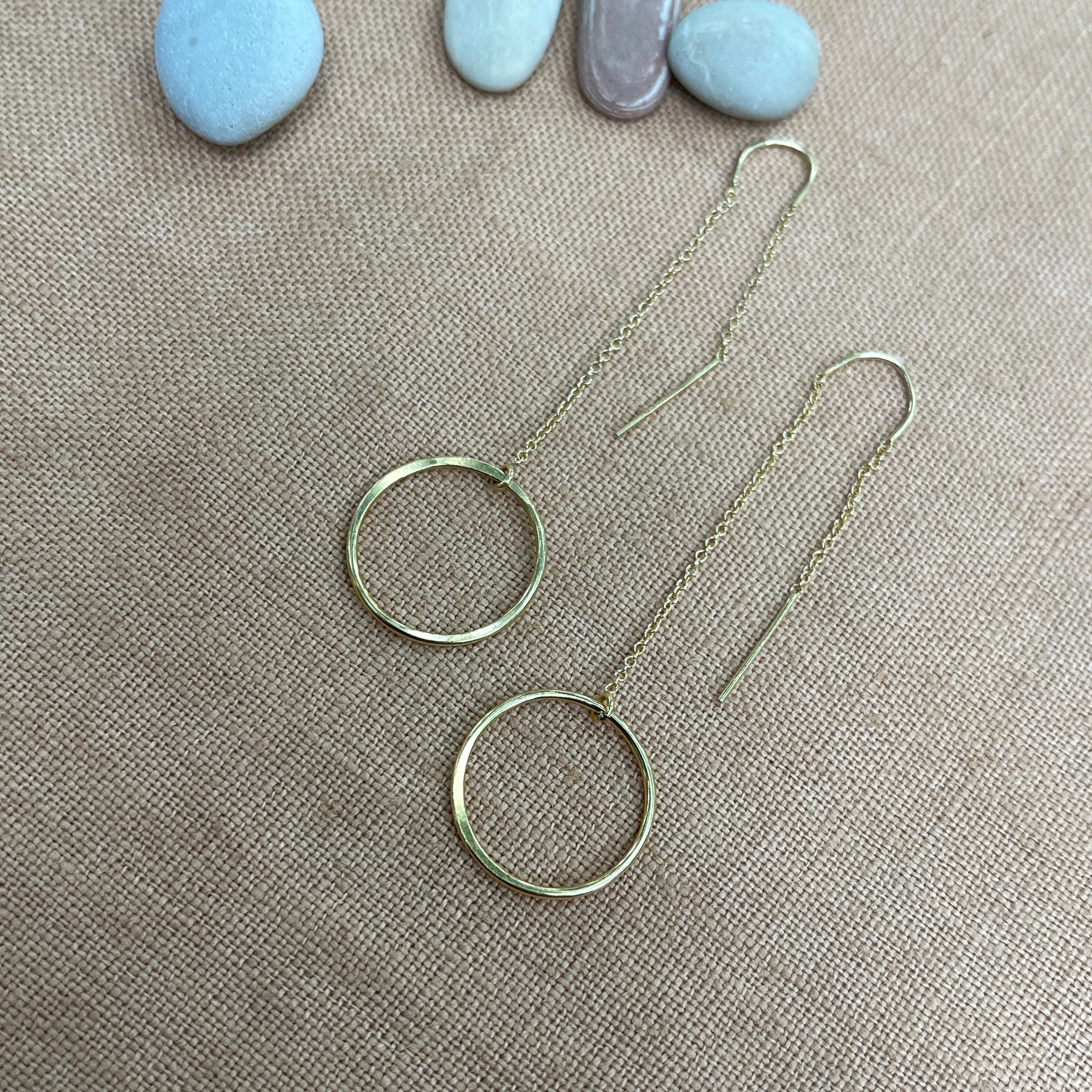 Silver hoop earrings on a textured beige surface with stones in the background
