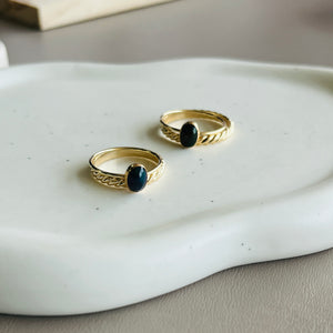 two gold rings with black stones on a white tray
