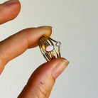 Hand holding a gold ring with an opal stone against a plain background