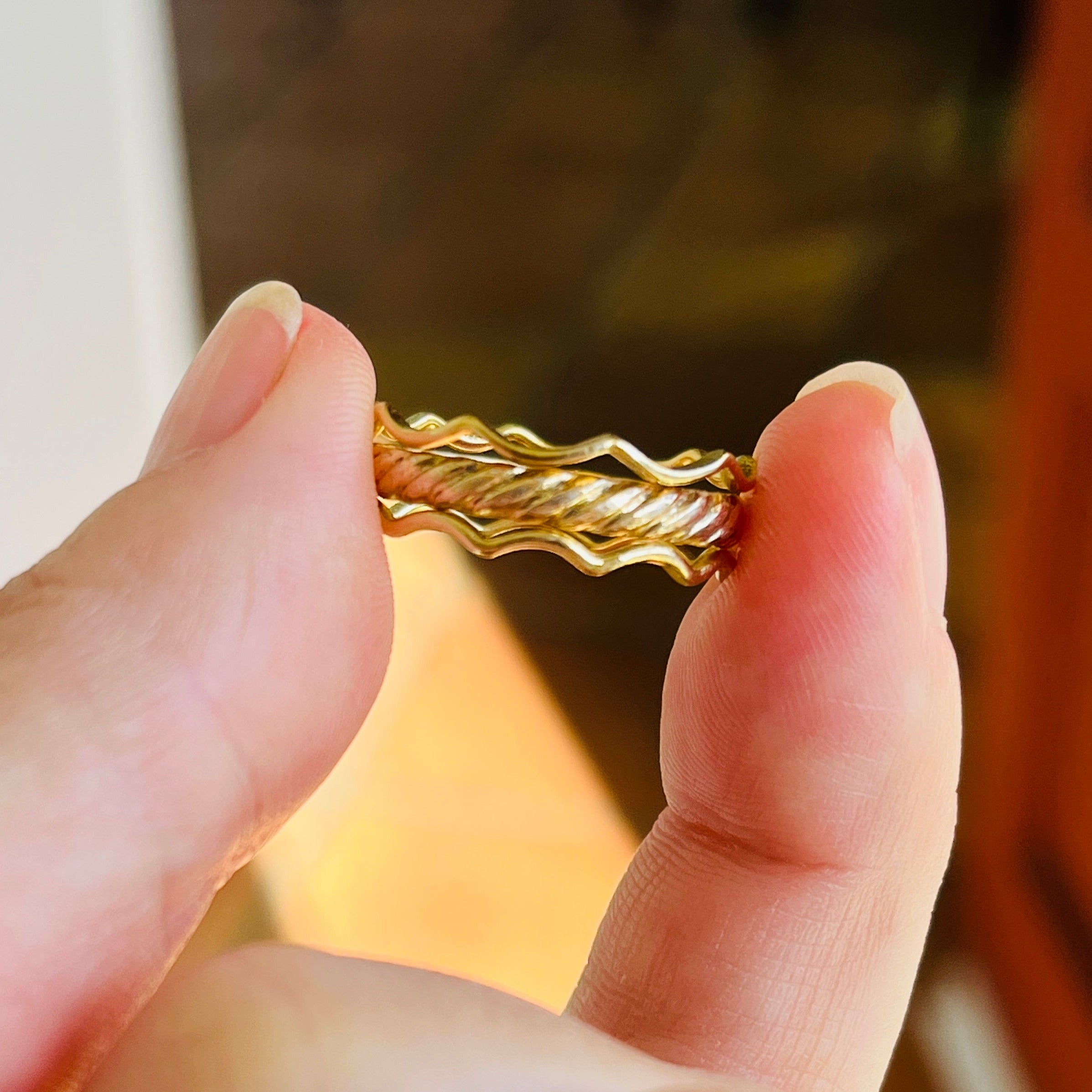 Gold bracelet being held between fingers with a blurred background