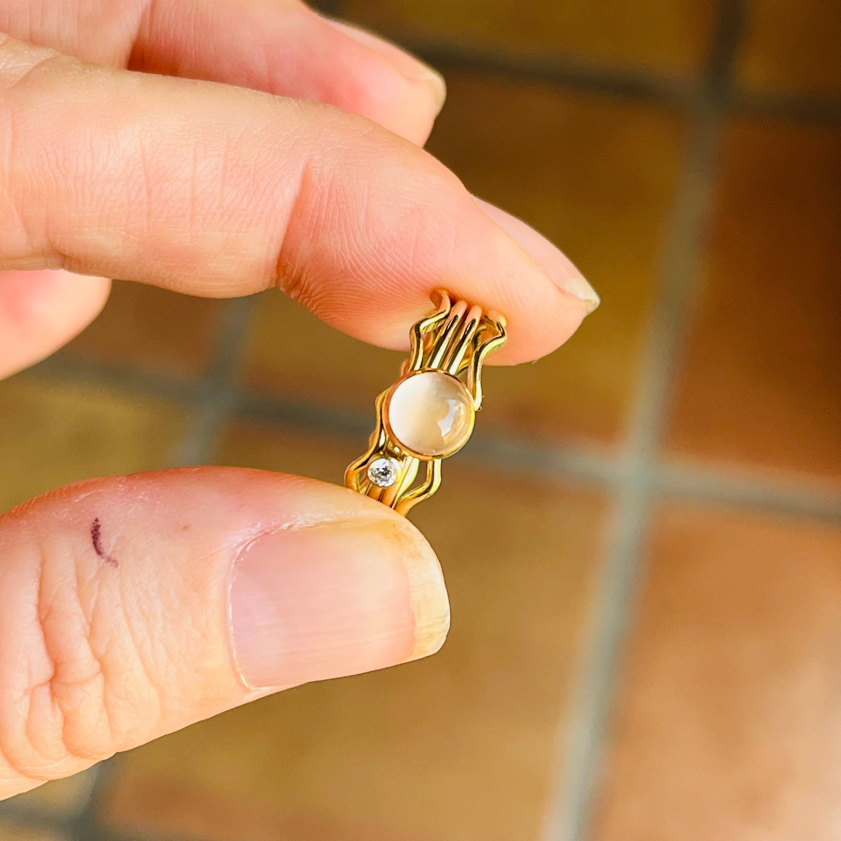 Gold earring with a pearl held between two fingers on a tiled floor background