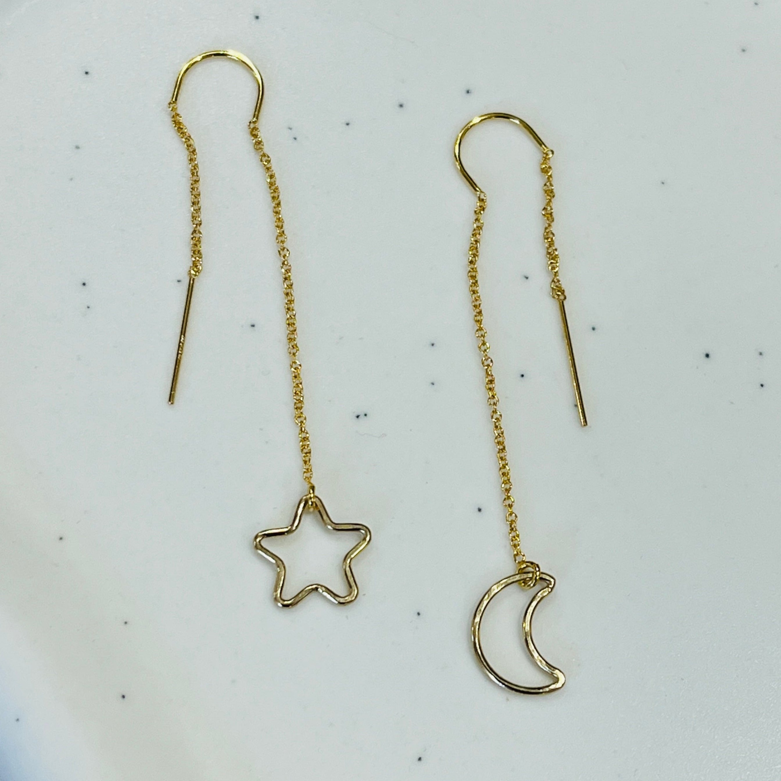Two earrings, one shaped like a star and the other like a crescent moon, both in gold color, placed on a white dish.
