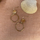 Gold hoop earrings on a textured beige surface with a shell in the background