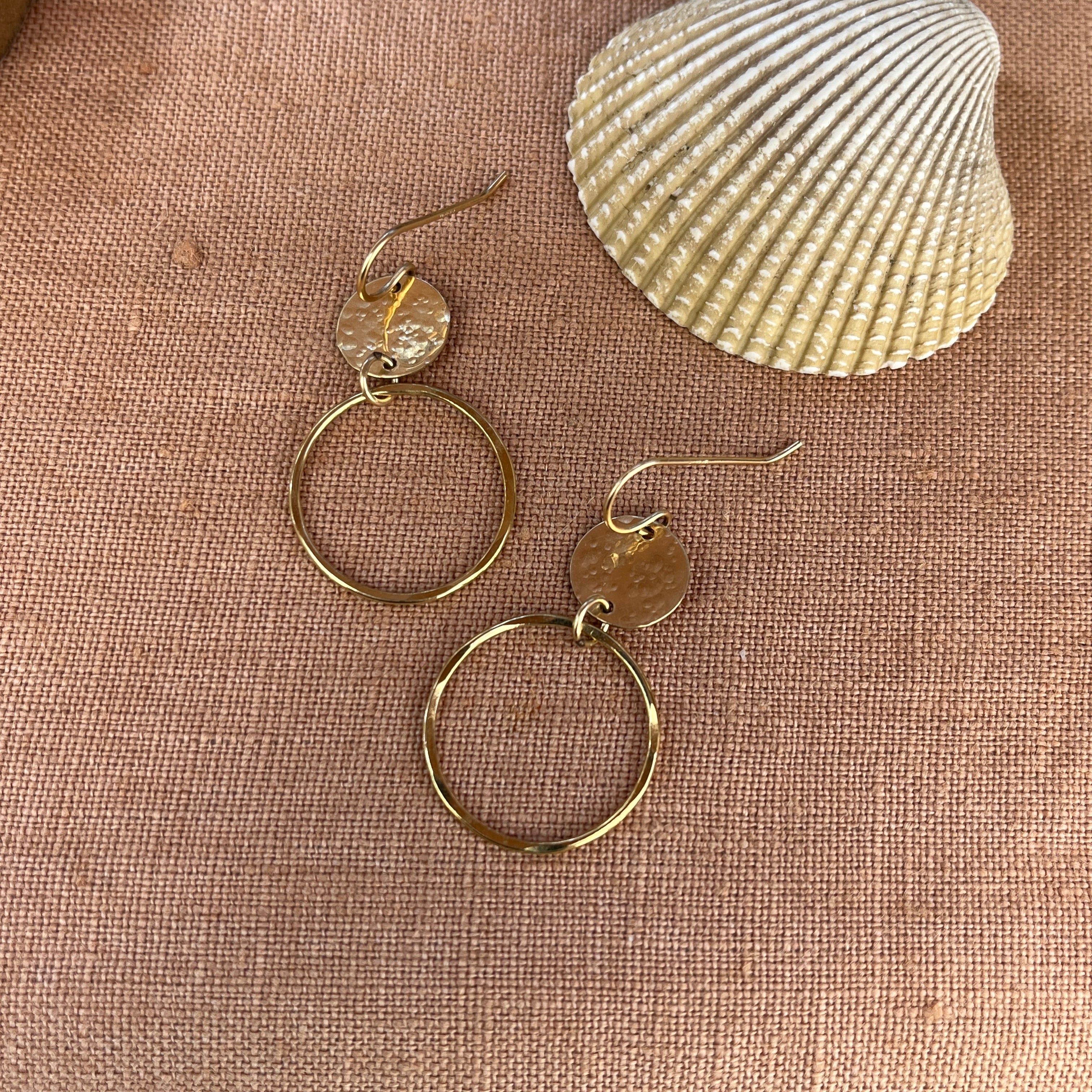 Gold hoop earrings on a textured beige surface with a shell in the background