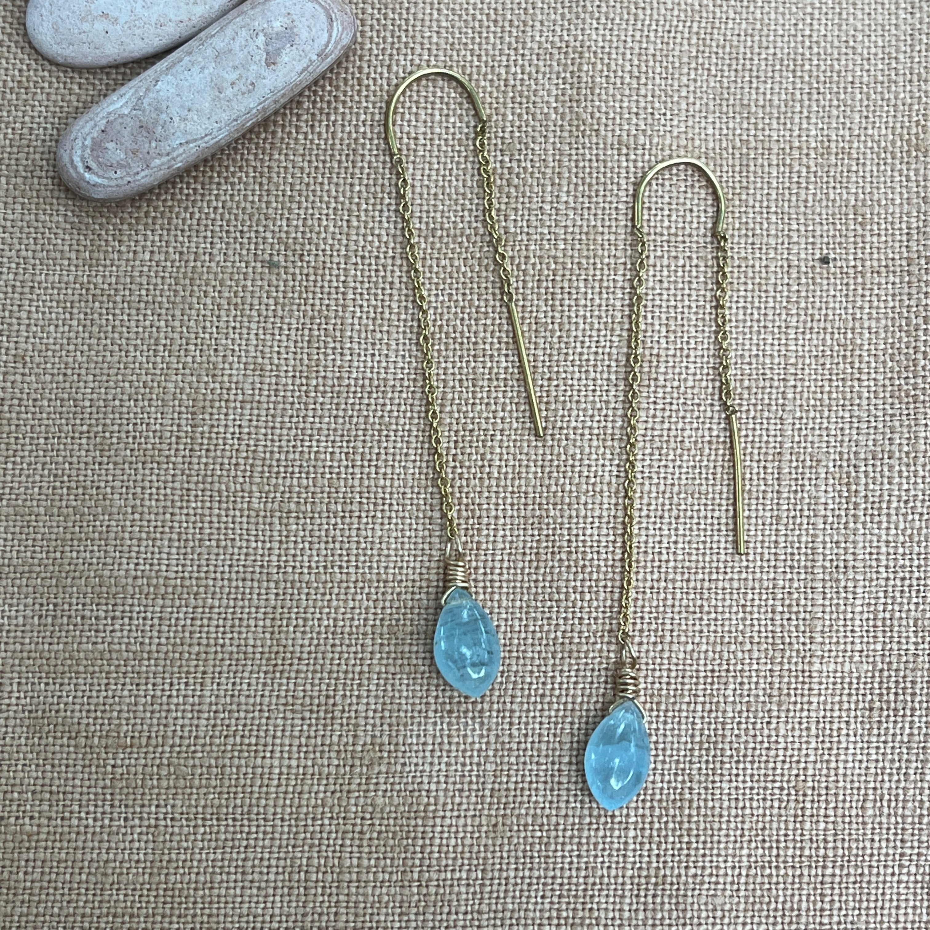 Threader earrings with blue gemstones on a textured fabric background
