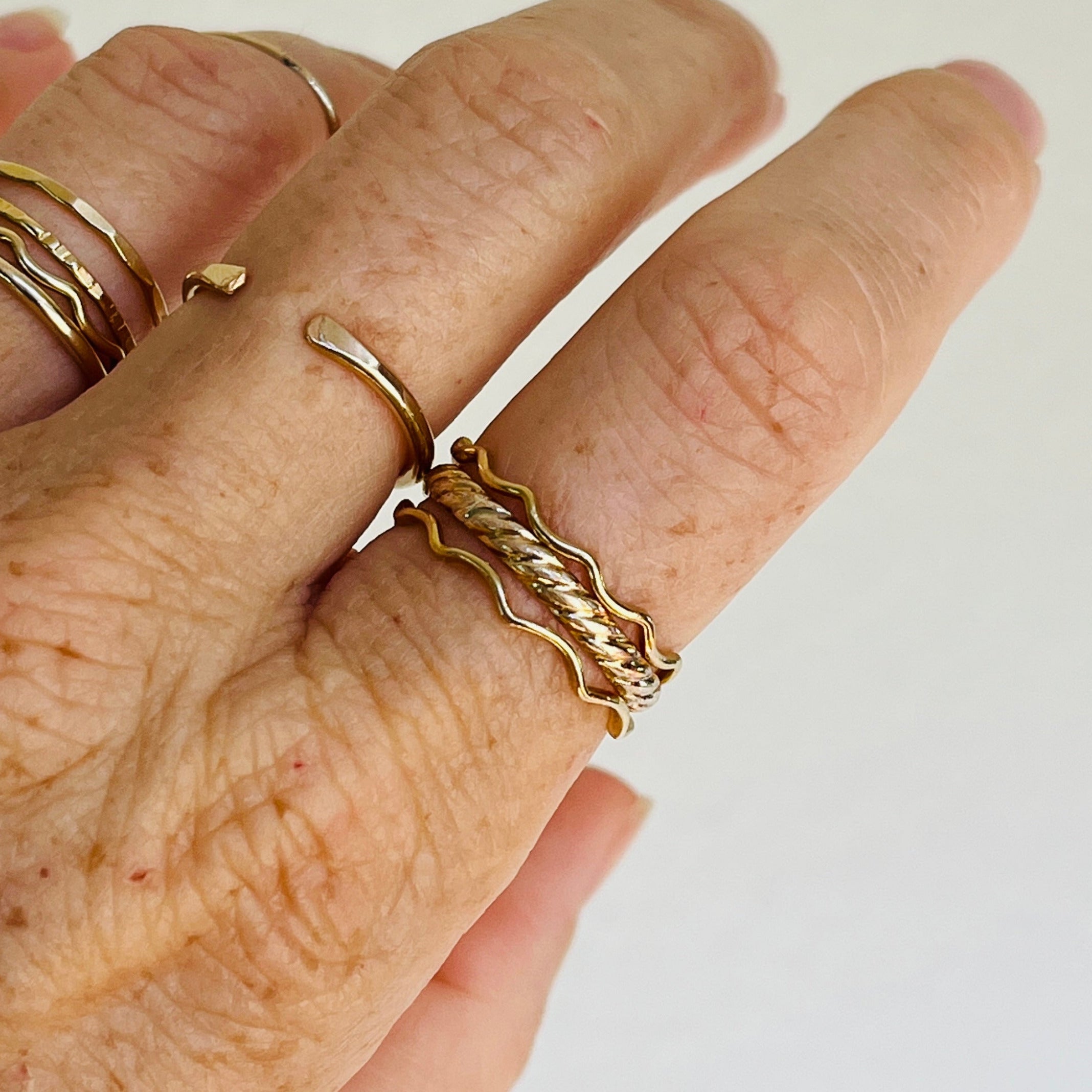 Hand wearing multiple gold rings on a plain background