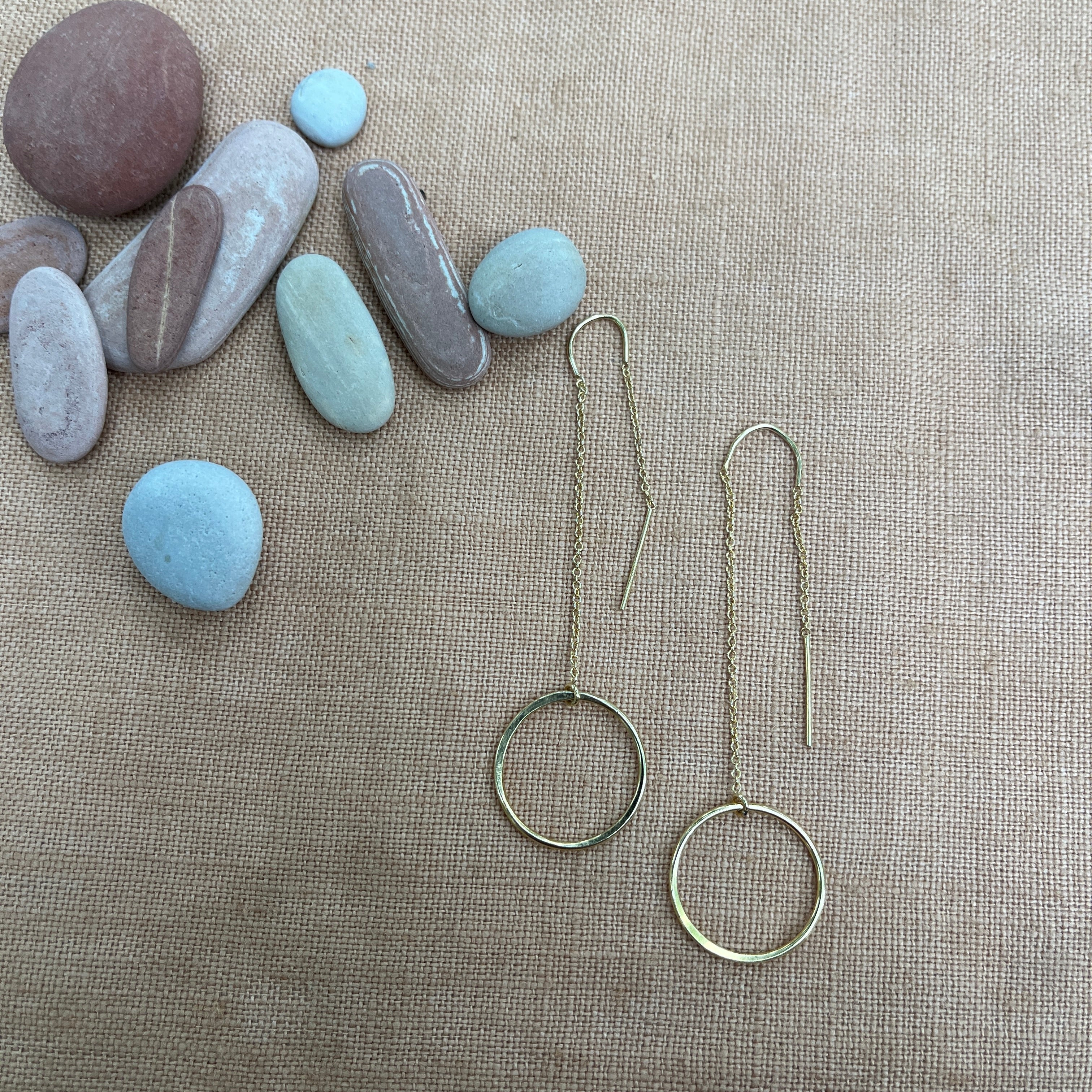Gold hoop earrings on a textured surface with stones in the background