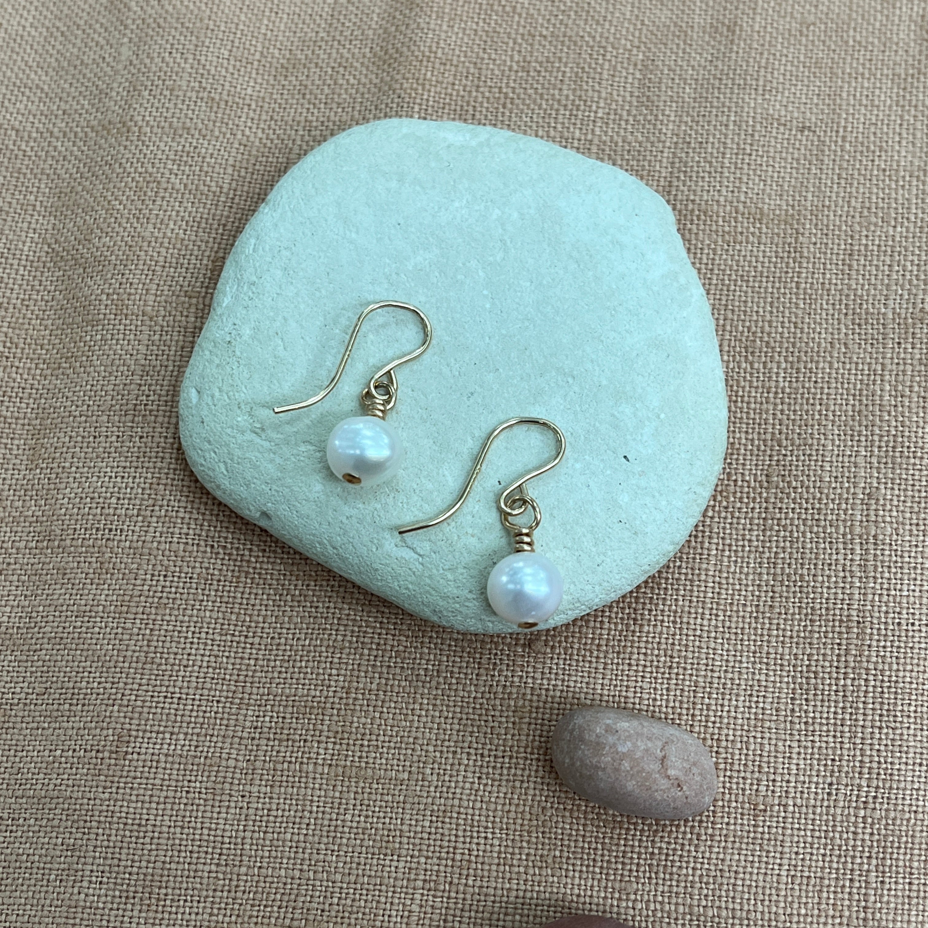Pearl earrings on a light blue stone with a beige background