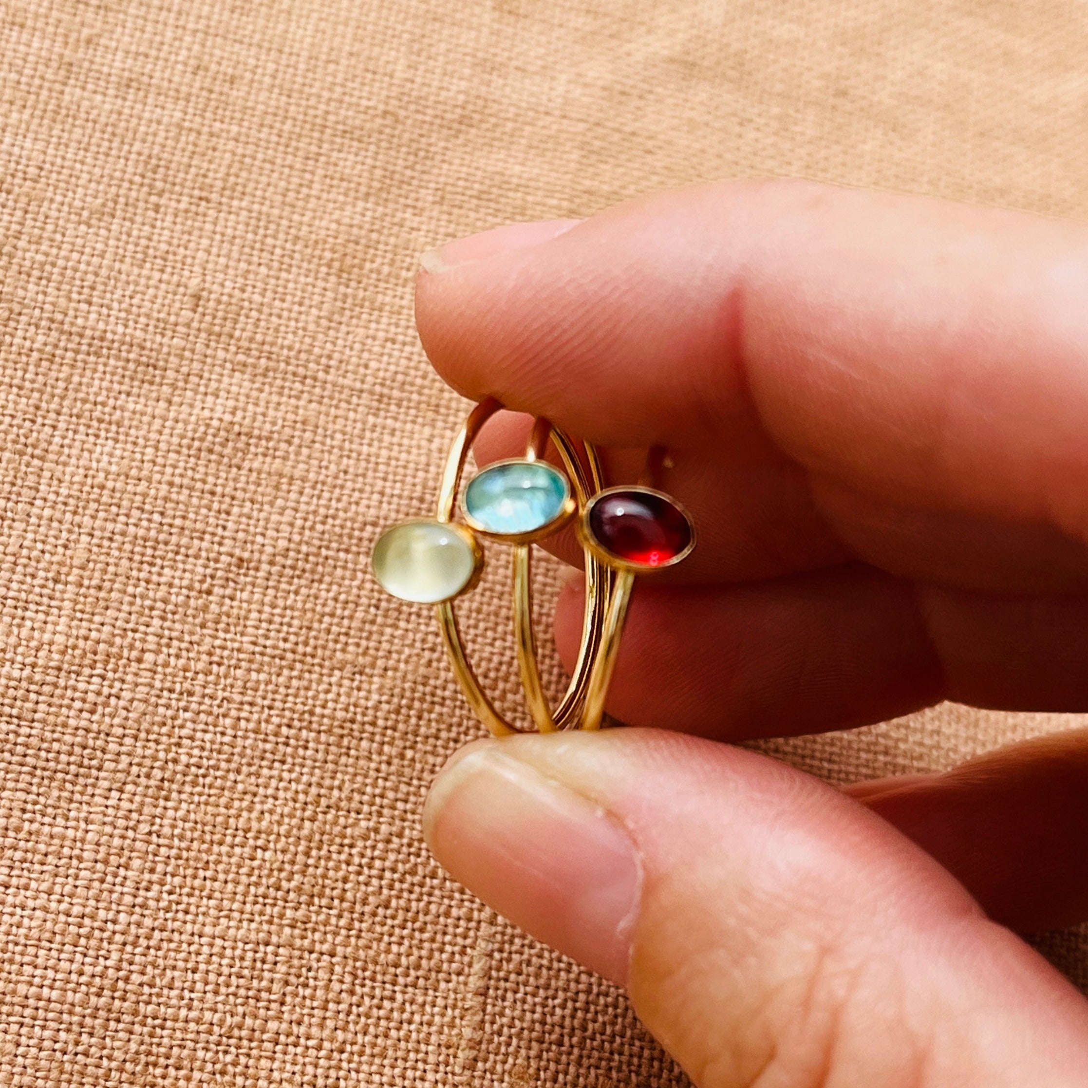 Gold ring with multicolored gemstones held between fingers on a beige fabric background