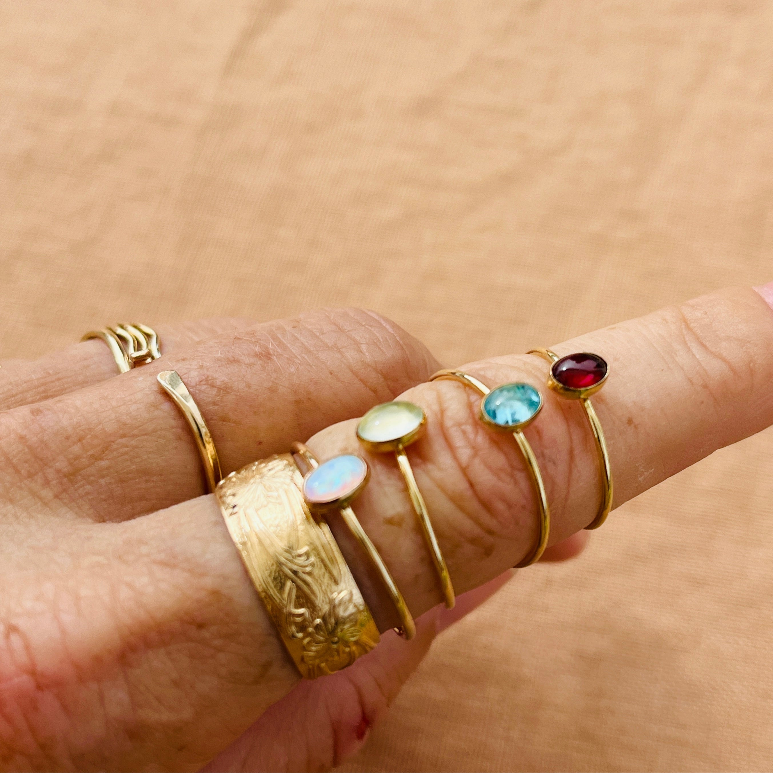 Hand wearing multiple gold rings with gemstones on a beige background