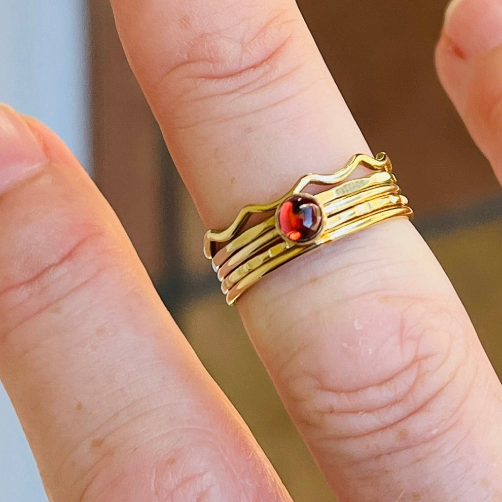 Gold ring with a red gemstone on a finger against a blurred background