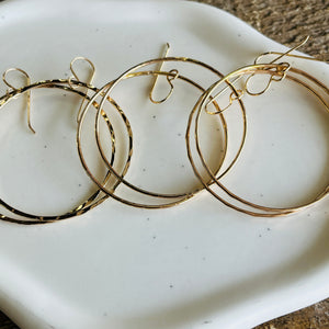 three pairs of gold hoop earrings on a white plate