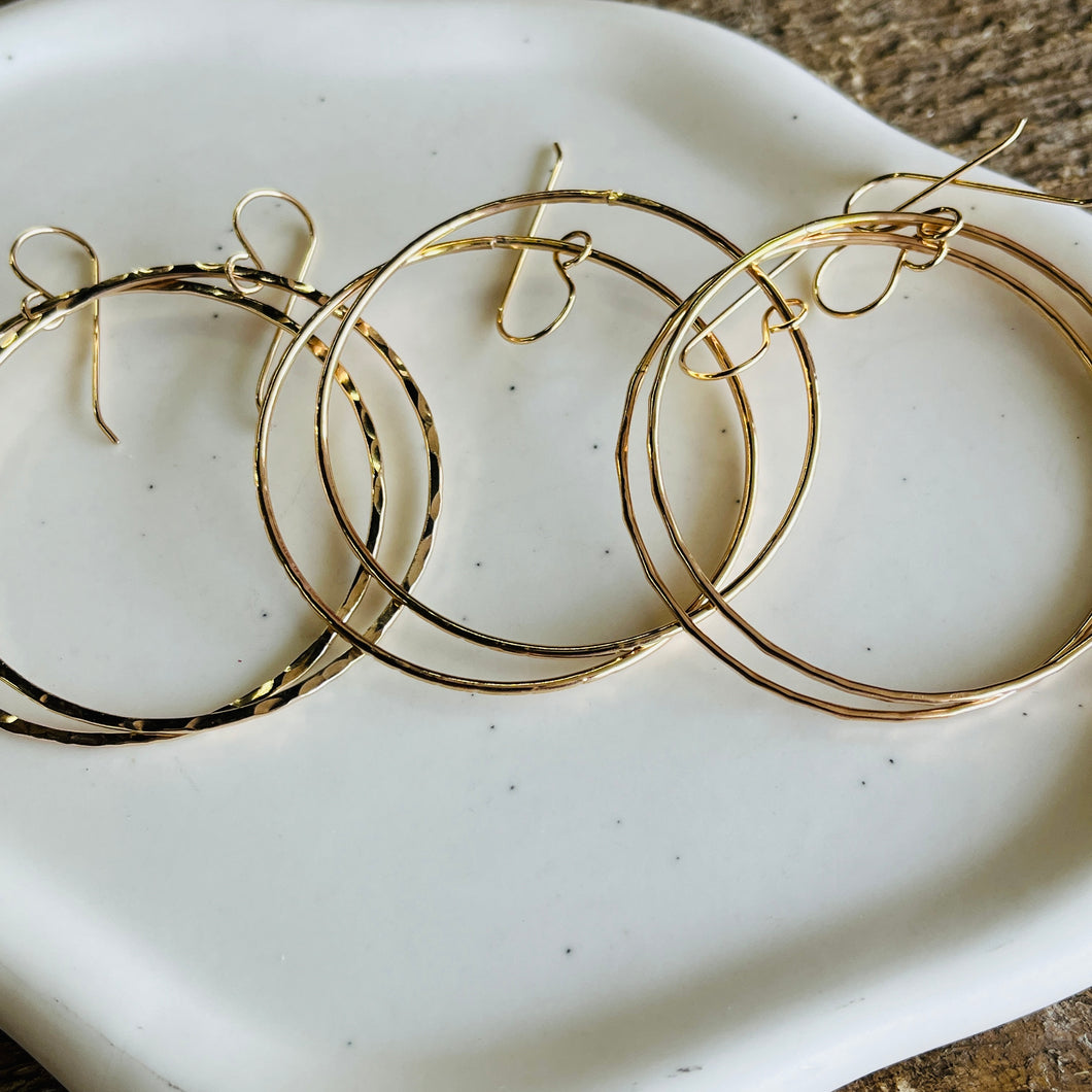 three pairs of gold hoop earrings on a white plate